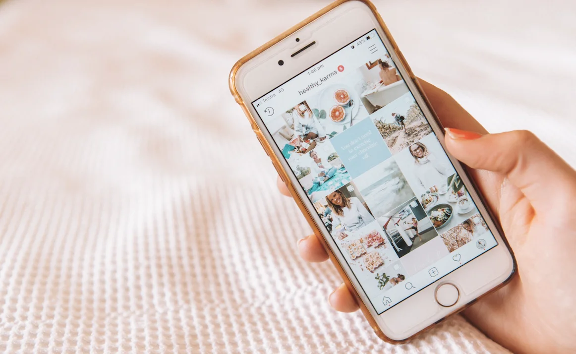 An image of a person's hand holding a phone displaying an Instagram feed.