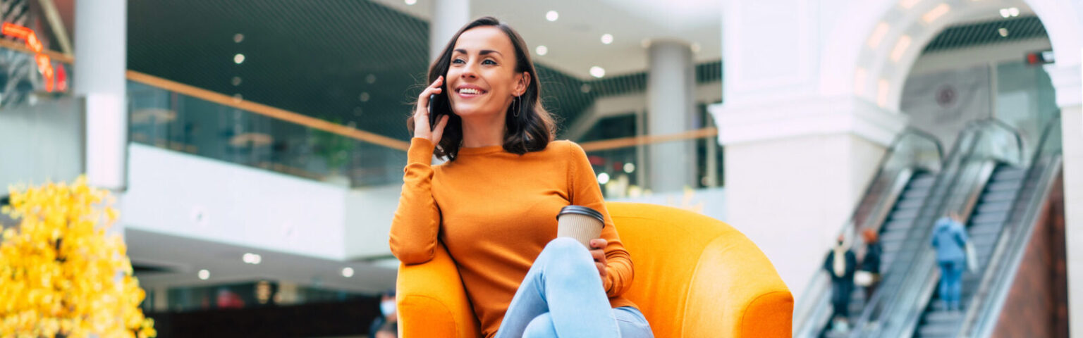 Beautiful trendy young woman with many colorful shopping bags in good mood with smart phone and credit card while sitting in the mall